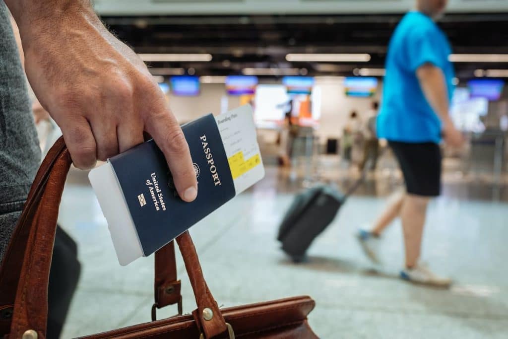 Homem segurando uma mala marrom, passaporte e passagem no aeroporto