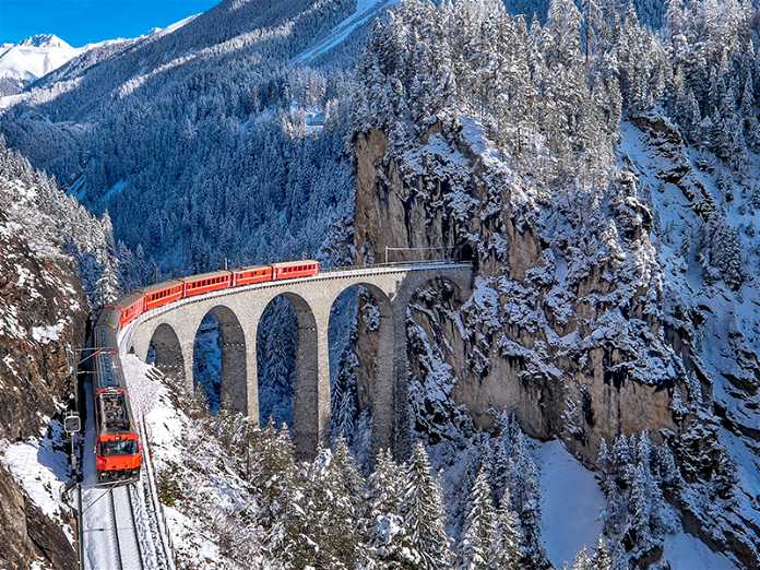 Trem andando sobre uma ponte com montanhas nevadas