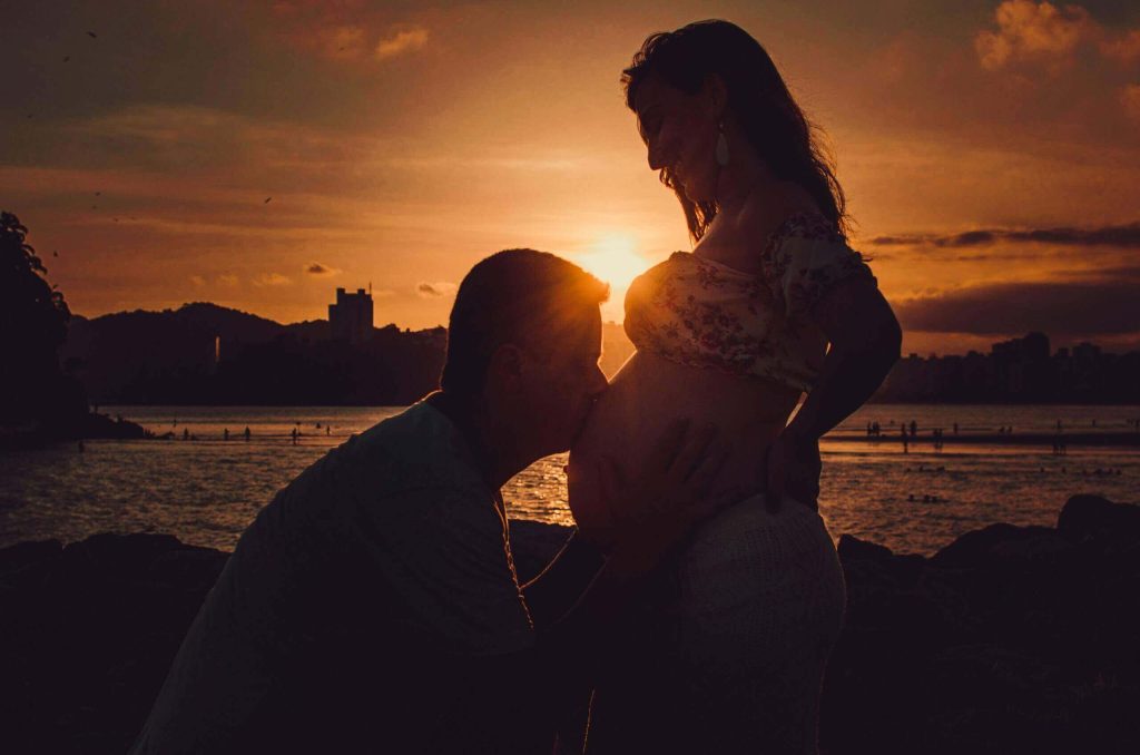 Homem beijando barriga de grávida durante uma babymoon.