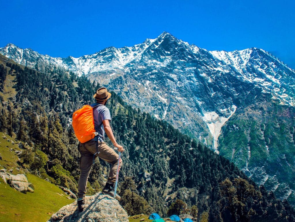 Homem vestindo camisa azul em pé no penhasco enquanto observa a montanha.